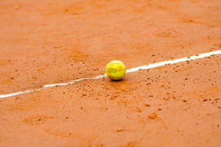 Tennis ball resting on a clay court, marked by a white line, ideal for sports themes.