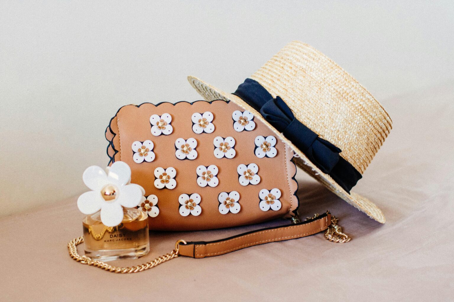 L’été 2026 s’accessoirise : collier plastron, ceinturon XXL et sac en cannage Chic ensemble featuring a floral handbag, straw hat, and perfume, perfect for summer fashion.