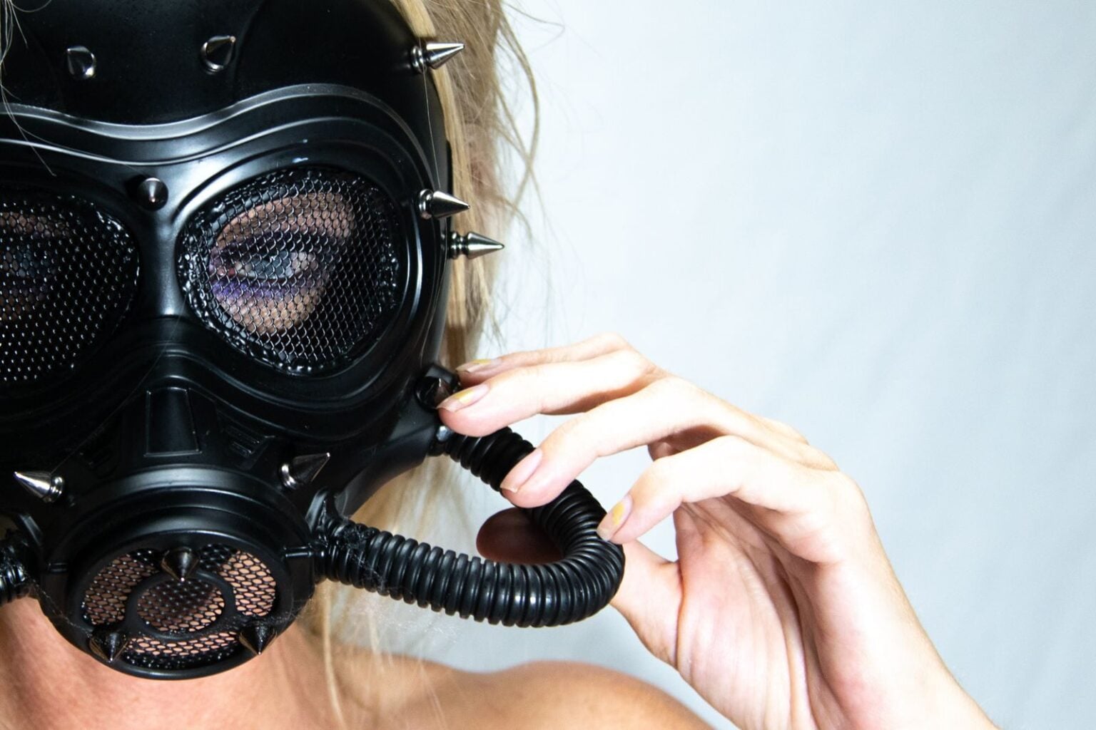 Close-up studio portrait of a woman in a spiked gas mask, showcasing edgy fashion.