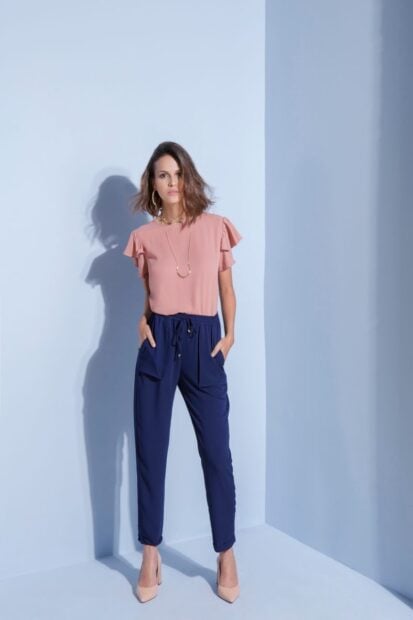 Elegant woman posing in pink blouse and navy pants against a light background, embodying contemporary fashion.