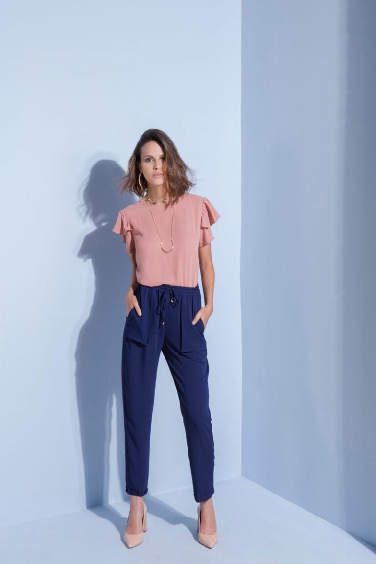 Elegant woman posing in pink blouse and navy pants against a light background, embodying contemporary fashion.