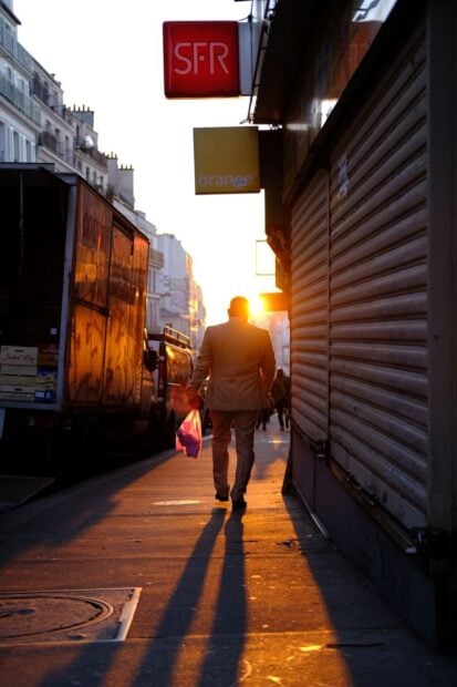 A silhouette of a man walking down a Parisian street during sunset, casting long shadows.