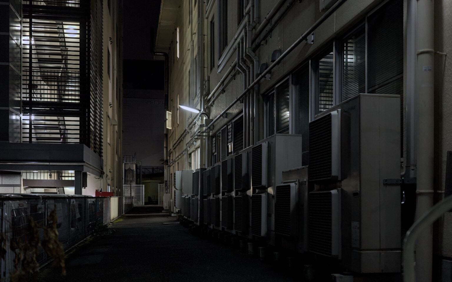 A dimly lit urban alley in Kyoto featuring air conditioning units, captured at night.