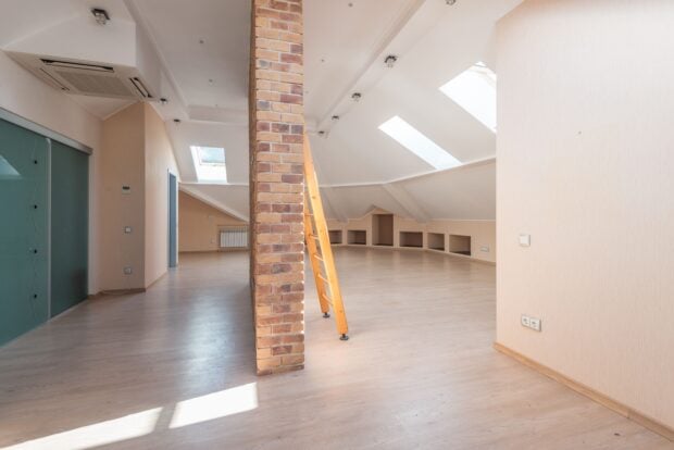 Occultant extérieur VELUX : le guide cash pour enfin rafraîchir vos combles Spacious attic room with natural light from skylights, featuring a brick pillar and a wooden ladder.
