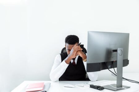 Réduire le stress quotidien : ce qui marche vraiment, ce qui ne sert à rien, et pourquoi 64 % des Français sont encore à bout A businessman sitting at a desk, appearing stressed while working at a computer in a bright office.