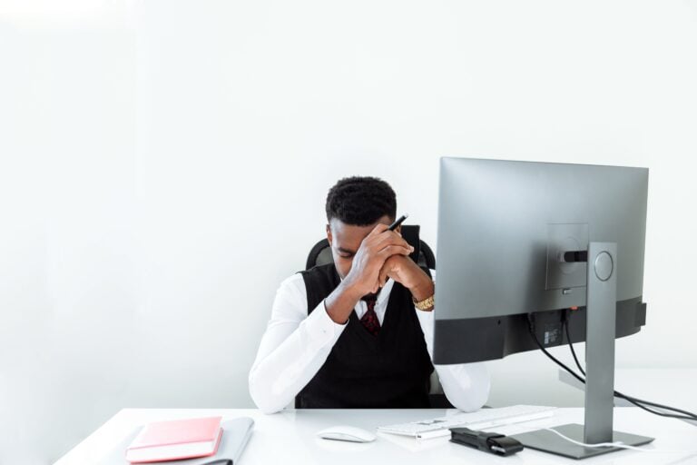 Réduire le stress quotidien : ce qui marche vraiment, ce qui ne sert à rien, et pourquoi 64 % des Français sont encore à bout A businessman sitting at a desk, appearing stressed while working at a computer in a bright office.