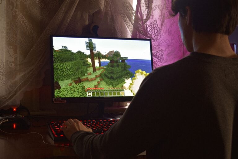 Serveurs Minecraft en 2026 : survivre, crafter, dominer et ne plus subir le lag A young man intensely playing a PC video game indoors. Capturing the essence of technology and concentration.