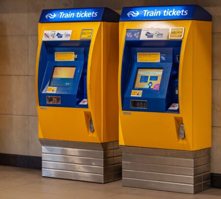 Vente flash SNCF : 100 000 billets TGV Inoui à 19 € pour août 2026 Two vibrant yellow and blue train ticket machines in an indoor station setting.