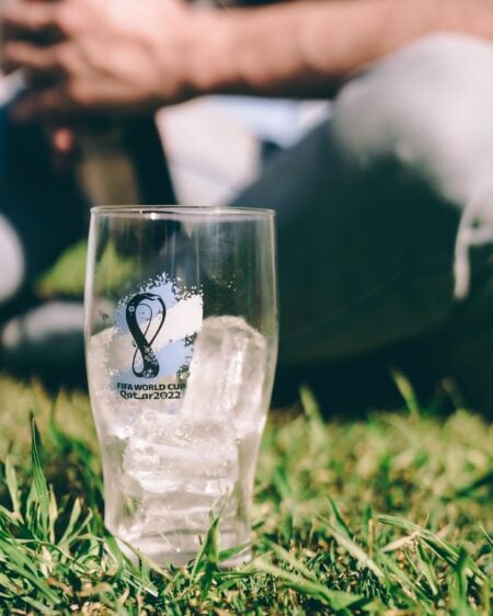 Nouvelles règles Coupe du monde 2026 : temps de jeu, VAR, comportements des joueurs et visas supporters Close-up of a glass with ice cubes on grass during a sunny outdoor event, FIFA World Cup 2022 branding visible.