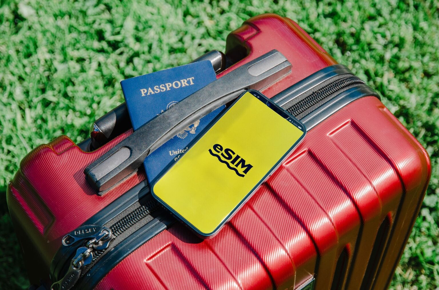 eSIM voyage 2026 : le piège de la eSIM sans numéro de téléphone, et comment l’éviter Close-up of a red suitcase with a smartphone displaying eSIM and a passport, symbolizing travel readiness.