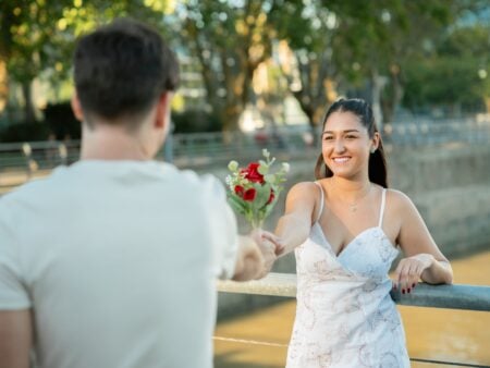 Réussir son premier rendez-vous : la méthode complète Young couple exchanging roses by the riverside in Buenos Aires, capturing a romantic moment.