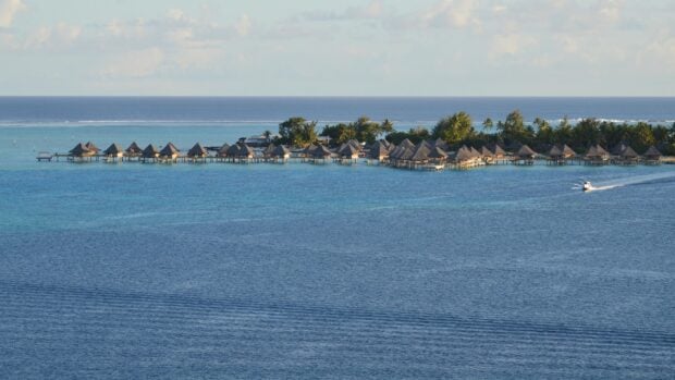 Overwater bungalows on a tropical island with clear blue sea and lush coast.