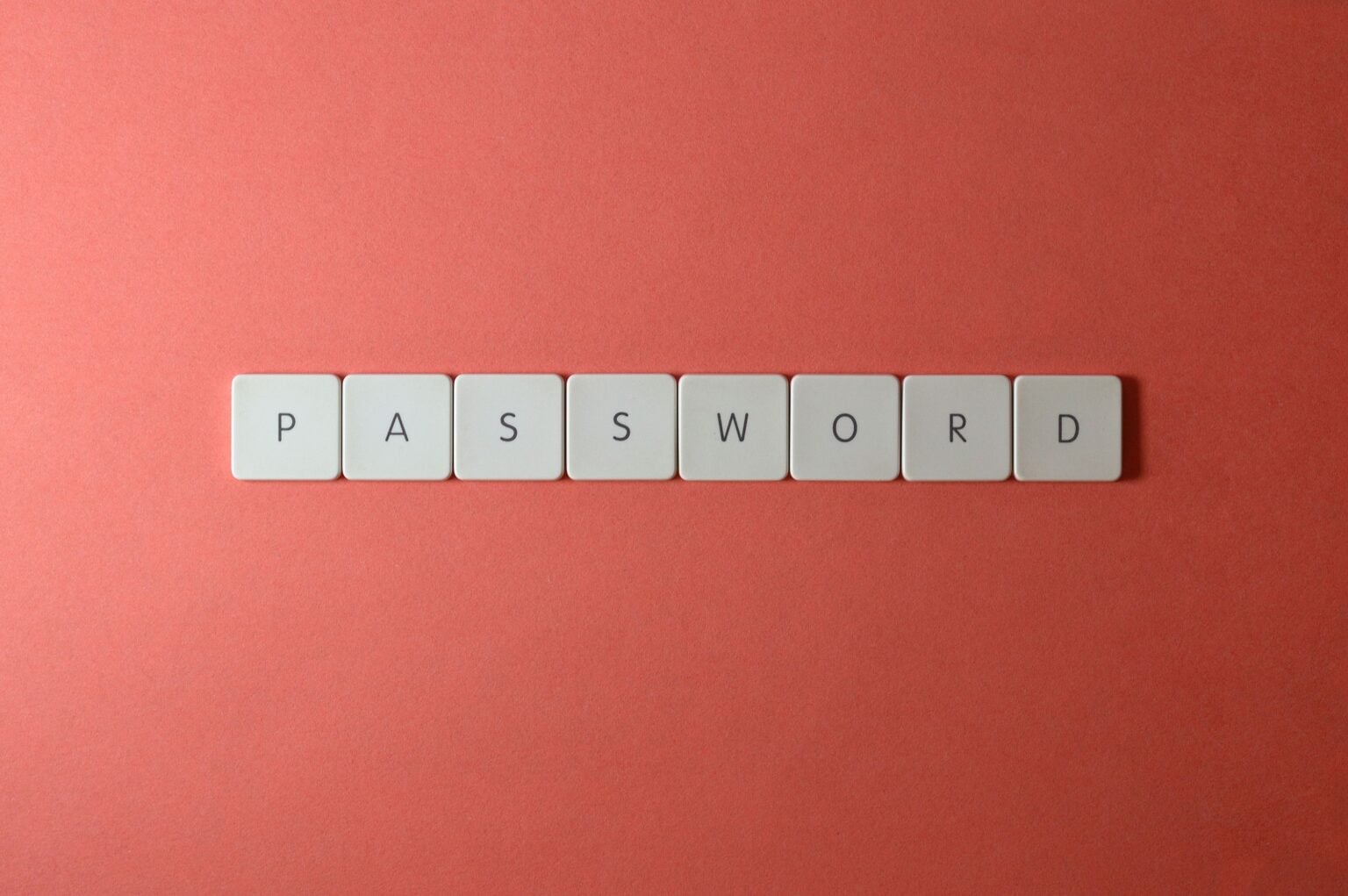 Gestionnaire de mot de passe : pourquoi 94% se font piéger et comment y échapper Focus on password security with white keyboard tiles spelling 'PASSWORD' on a coral background.