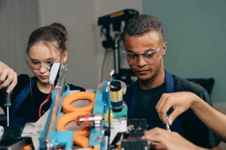 Two young engineers focusing on a robotics project indoors, showcasing teamwork and technology.