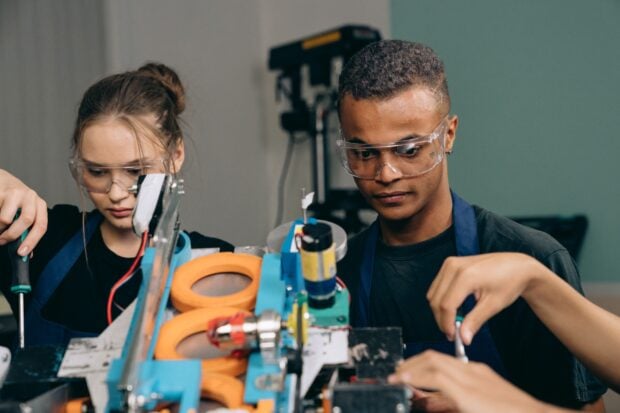 Métiers de la Robotique en 2026 : Pourquoi ce Secteur Recrute en Masse (et Paie Très Bien) Two young engineers focusing on a robotics project indoors, showcasing teamwork and technology.