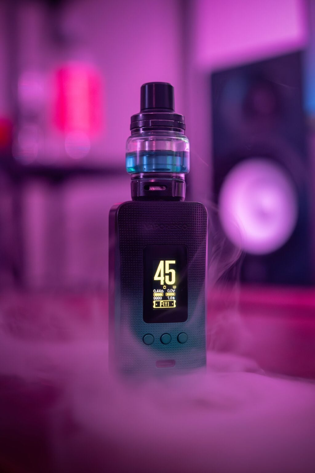 Close-up of an electronic vape device with illuminated screen and surrounding vapor, set against a purple-lit background.