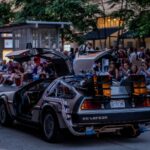 A DeLorean car at a street parade in Minneapolis with a crowd watching.