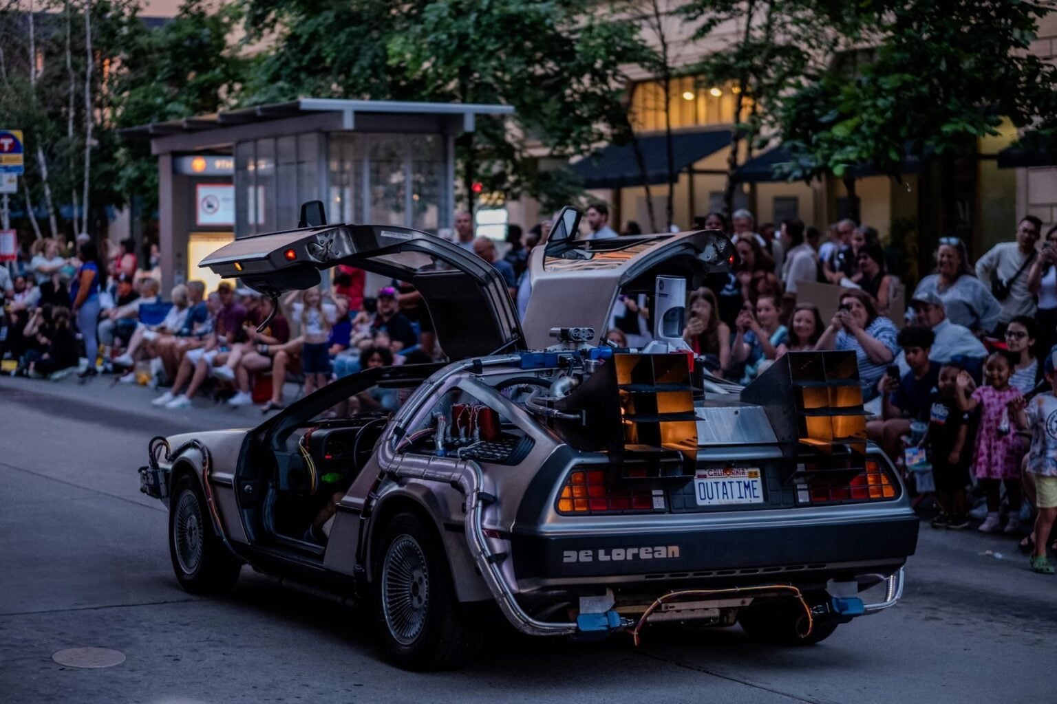 Les voitures les plus emblématiques du cinéma : ces bagnoles qui ont volé la vedette aux humains A DeLorean car at a street parade in Minneapolis with a crowd watching.