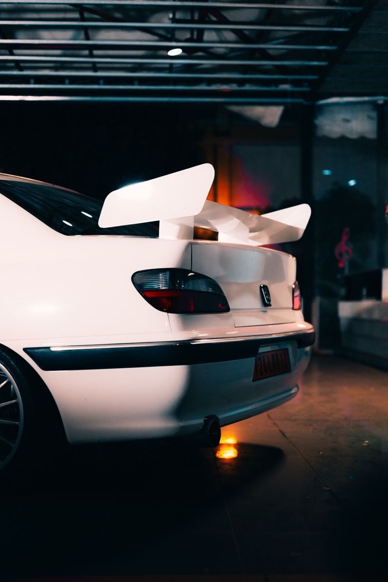 Modern white sports car with distinctive rear spoiler, parked in a dimly lit garage setting.