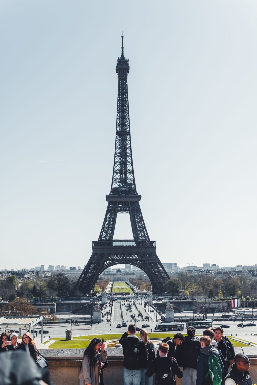 Visiter la tour Eiffel en 2026 : le guide pratique pour éviter la file Visitors gather near the Eiffel Tower in Paris on a clear day, showcasing iconic architecture.