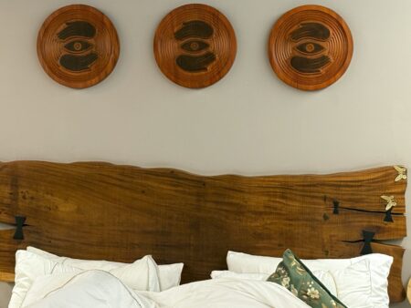 L’esthétique du bois brut dans le design d’intérieur contemporain Three wooden wall hangings above a bed