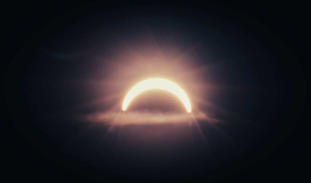 A bright crescent sun partially obscured by a dark cloud in the sky.
