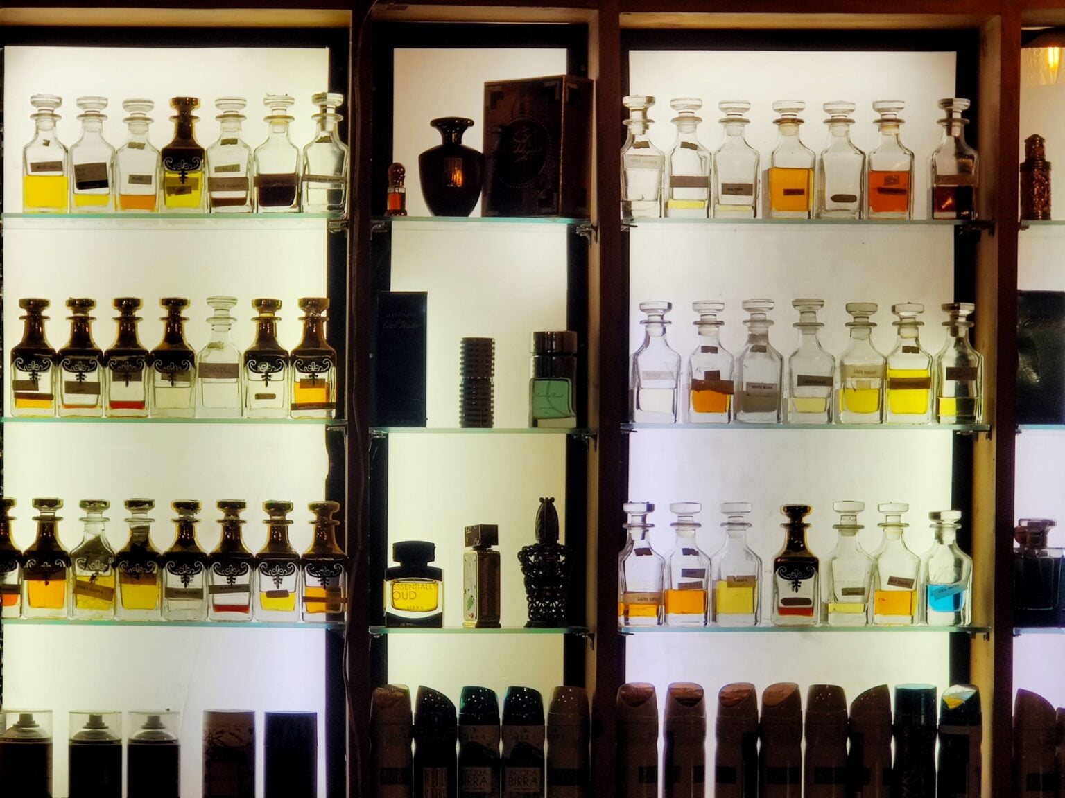 Parfum de niche : pourquoi il est devenu un sujet de conversation à part entière Aesthetic arrangement of diverse perfume bottles on illuminated shelves showcasing luxury fragrances.
