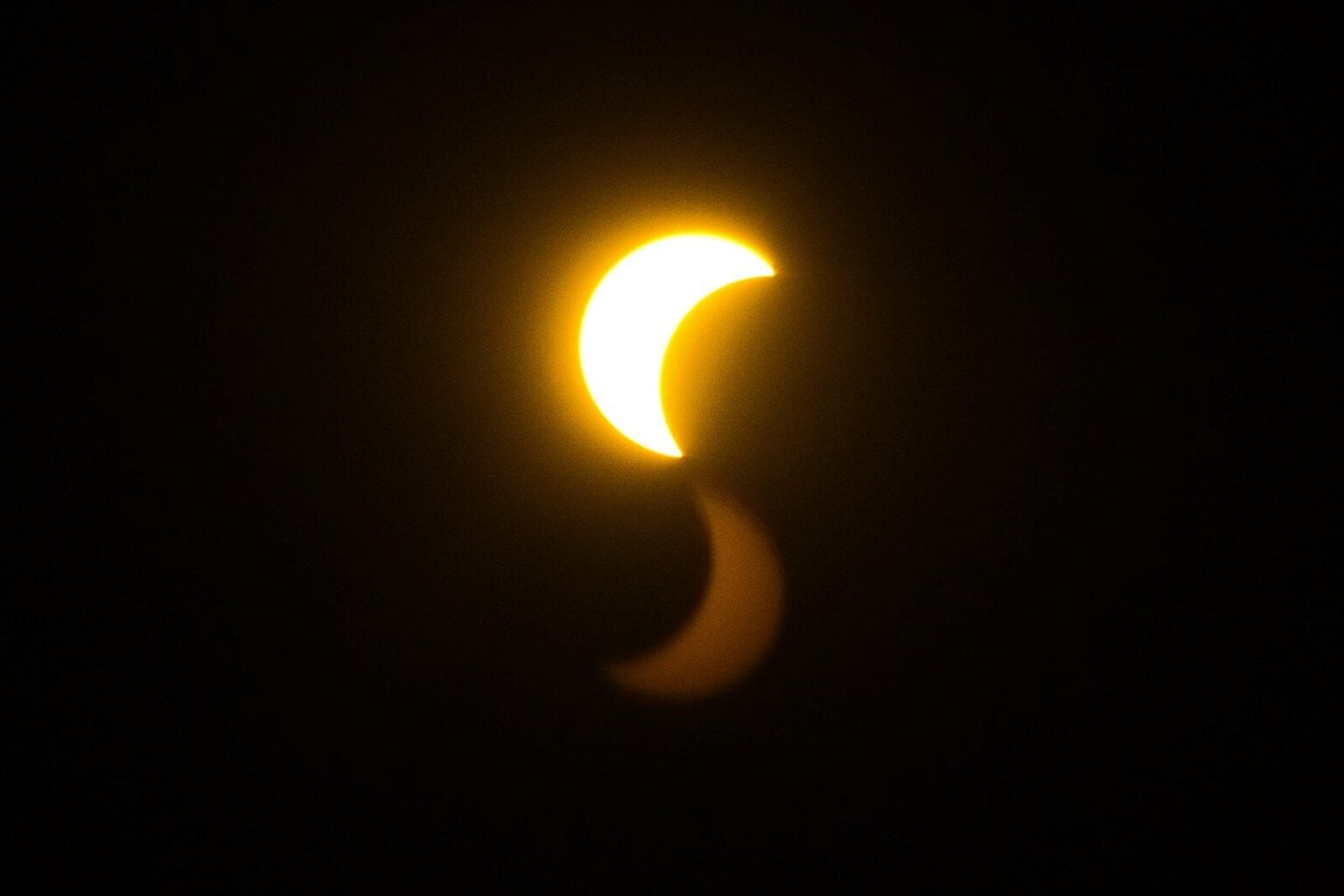 Comment savoir si l’éclipse a abîmé vos yeux : les signes qui comptent A bright crescent sun with a faint reflection against a black sky.