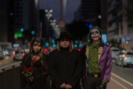 Halloween 2026 : les déguisements cinéma qui vont cartonner, et comment éviter le costume sous cellophane A trio in Halloween-themed cosplay walking through a bustling city street at night.