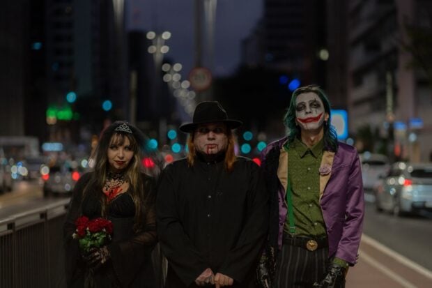 Halloween 2026 : les déguisements cinéma qui vont cartonner, et comment éviter le costume sous cellophane A trio in Halloween-themed cosplay walking through a bustling city street at night.