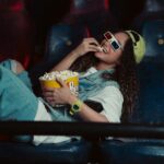 a woman sitting in a chair eating popcorn and watching a movie