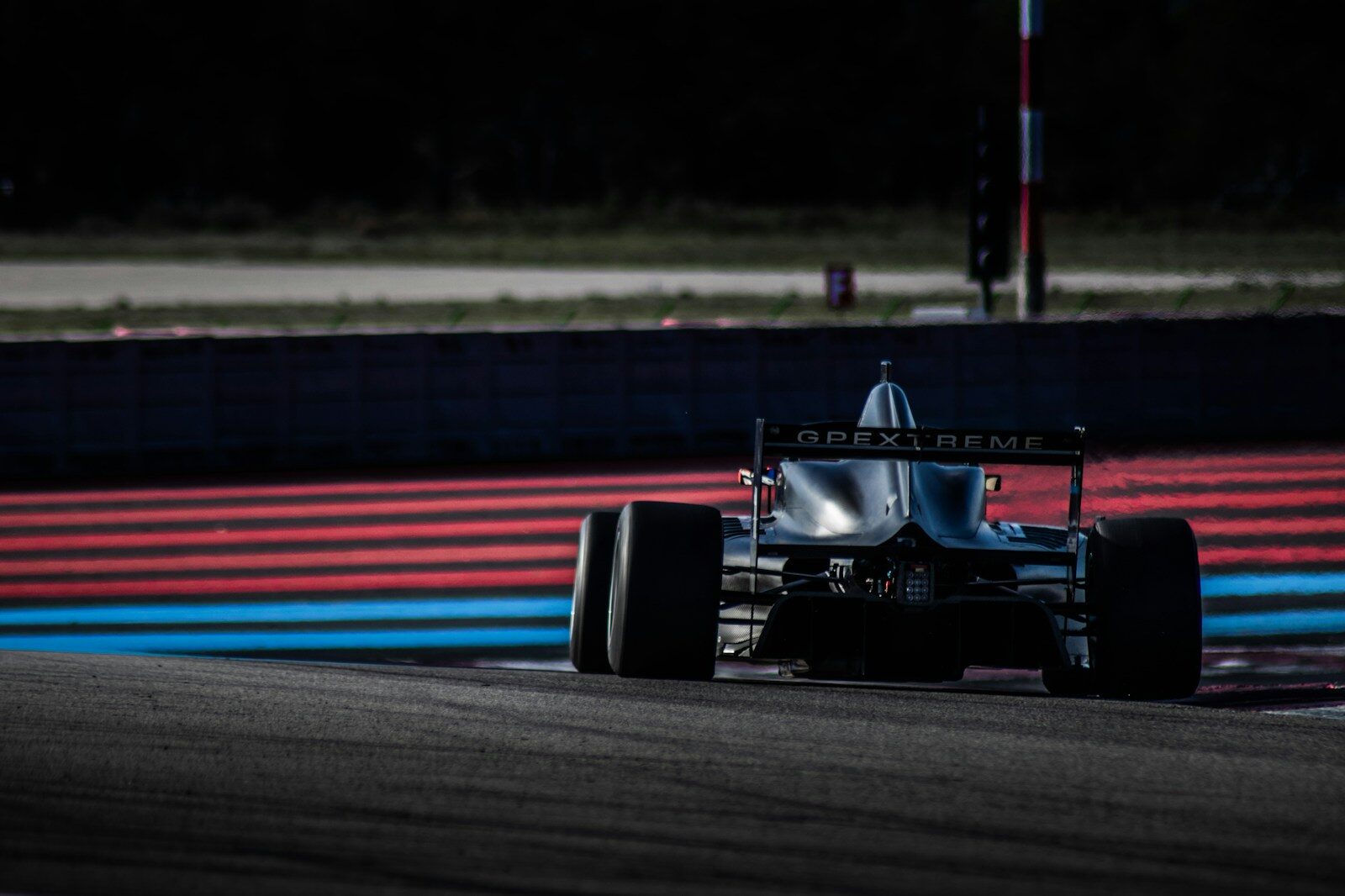 A black race car on a track with red and blue painted curbs