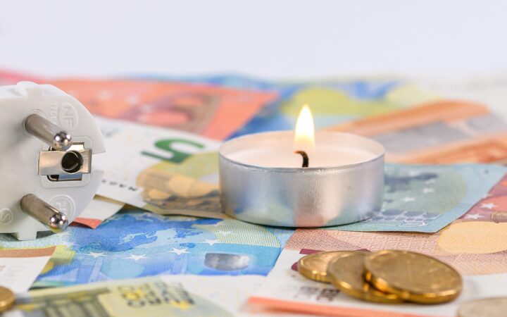 A burning candle on Euro money with a power plug symbolizing energy costs.