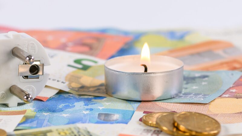 A burning candle on Euro money with a power plug symbolizing energy costs.